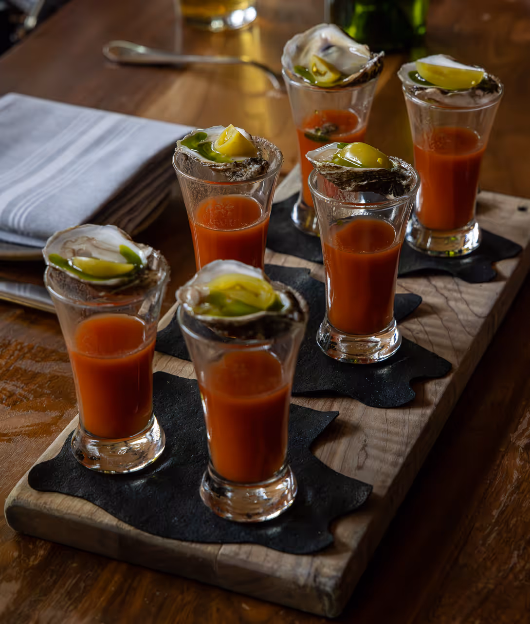 Michelada shot with oyster and citrus garnish on wooden table.