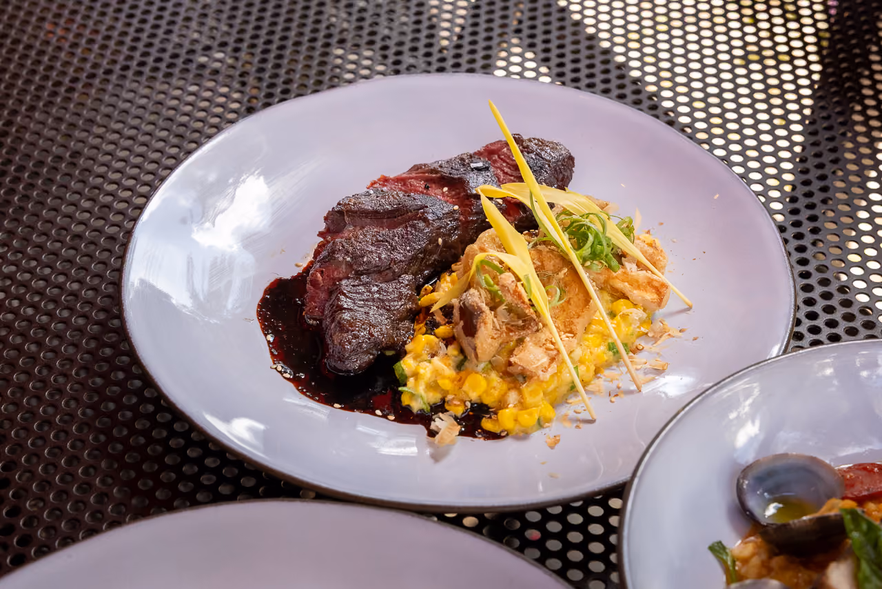 Gourmet ribeye steak with roasted vegetables and charred greens on a rustic plate.