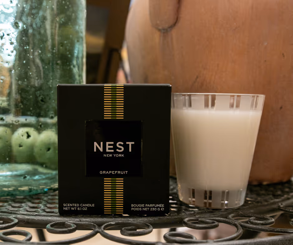 NEST New York Grapefruit scented candle box next to a filled glass candle holder on a decorative metal table.