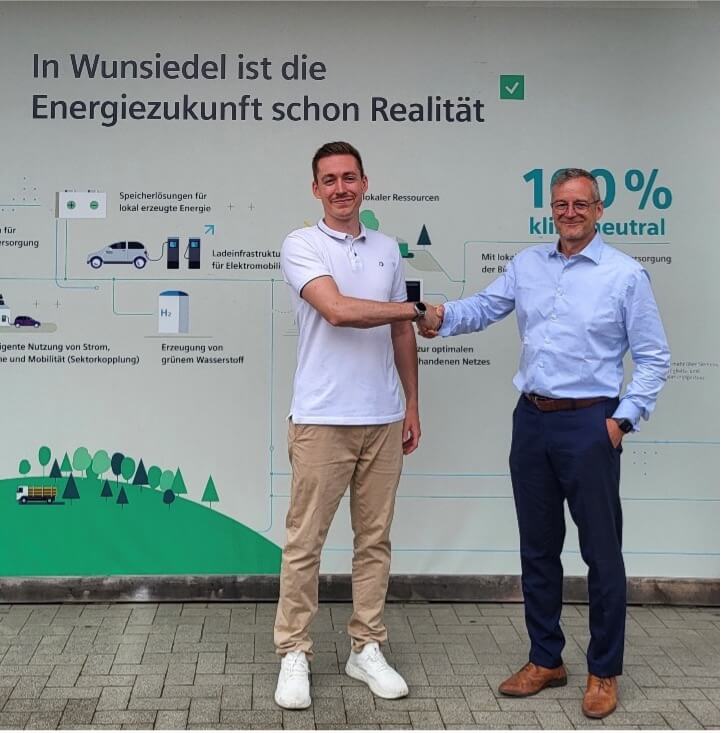 Der erste ZENERGIE-Mitarbeiter Rainer Härtl und ZENOB-Geschäftsführer Marco Krasser schütteln sich gegenseitig die Hand. Auf einer Wand im Hintergrund steht der Satz "In Wunsiedel ist die Energiezukunft schon Realität".