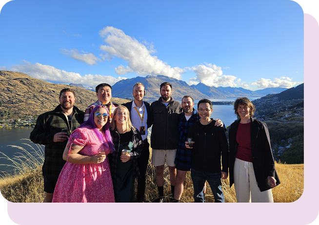 A group of people smiling at the camera, posed outdoors with the sky in the background.