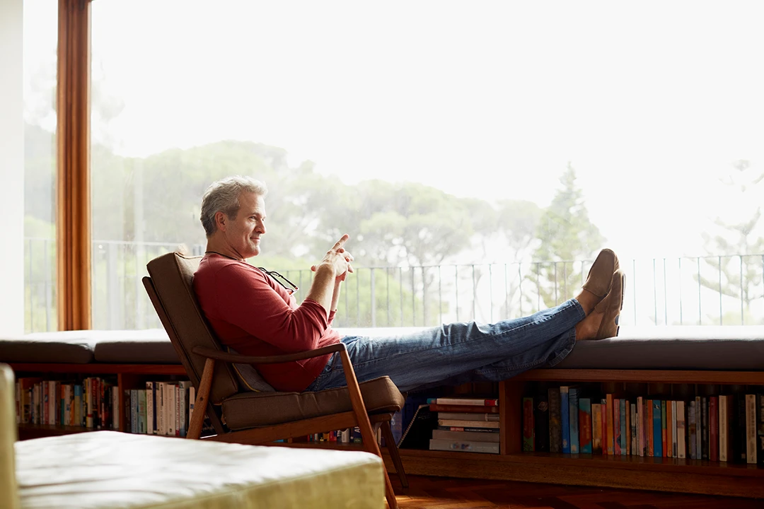A man sitting in a chair with his feet up smiling and looking out a large window.