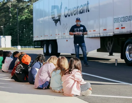 A man standing in front of a semi truck speaking to children