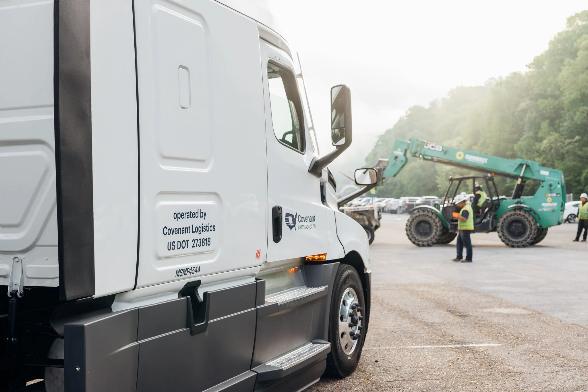 A white semi truck with workers and construction vehicles in the distance