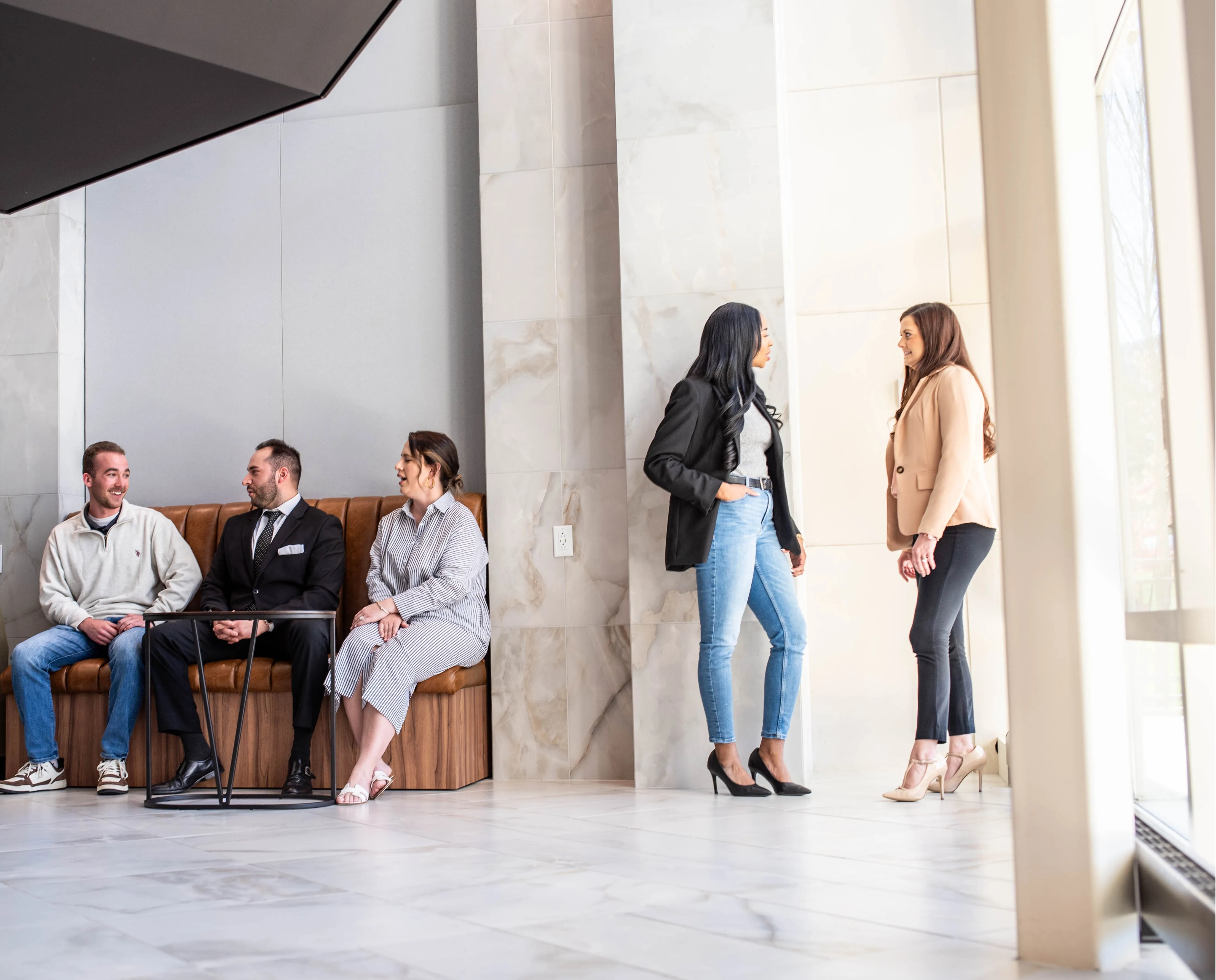 Three men sitting on a bench in a lobby with two women standing and talking to each other