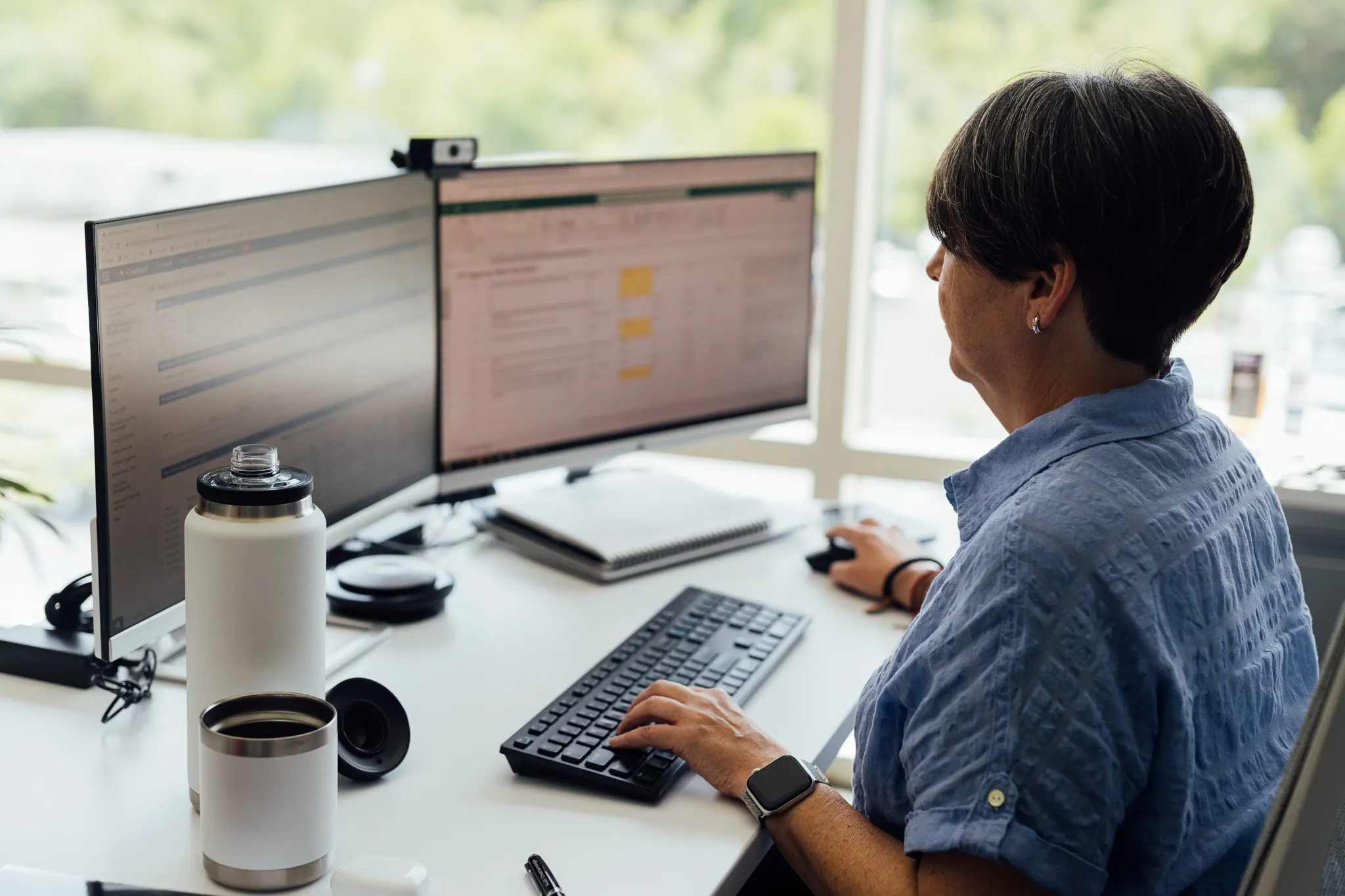 A woman sitting at a desk with a dual monitor setup