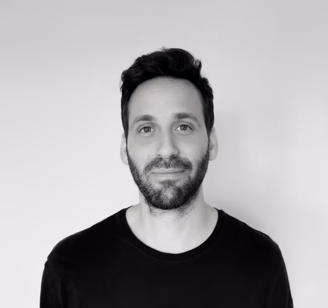 Portrait d’un homme avec barbe et cheveux foncés, souriant légèrement, sur fond clair.