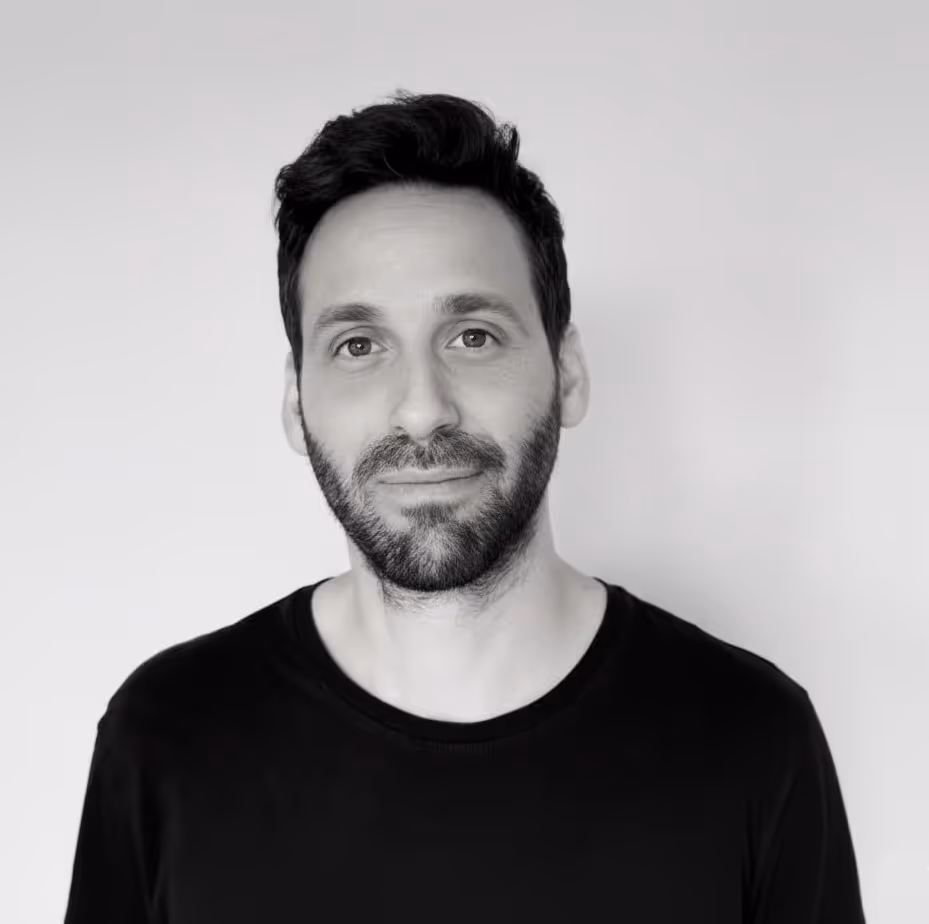 Portrait d’un homme avec barbe et cheveux foncés, souriant légèrement, sur fond clair.