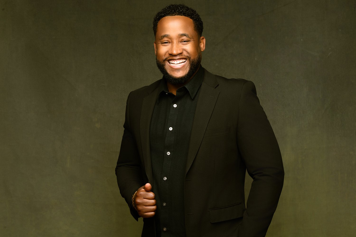 Chicago DJ smiling in a professional studio portrait, dressed in a tailored black suit