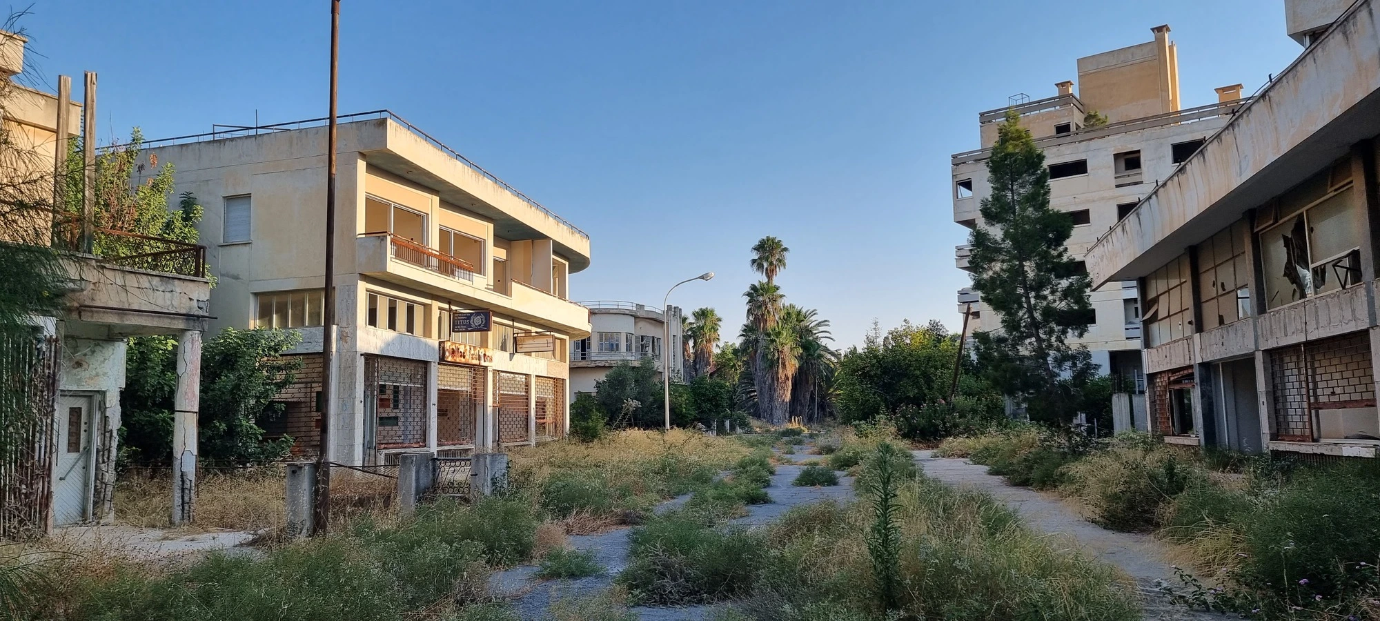 grass and trees overgrown and nature taking over the buildings over time, building windows broken, crumbling walls and rust in places, famagusta ghost town, cyprus
