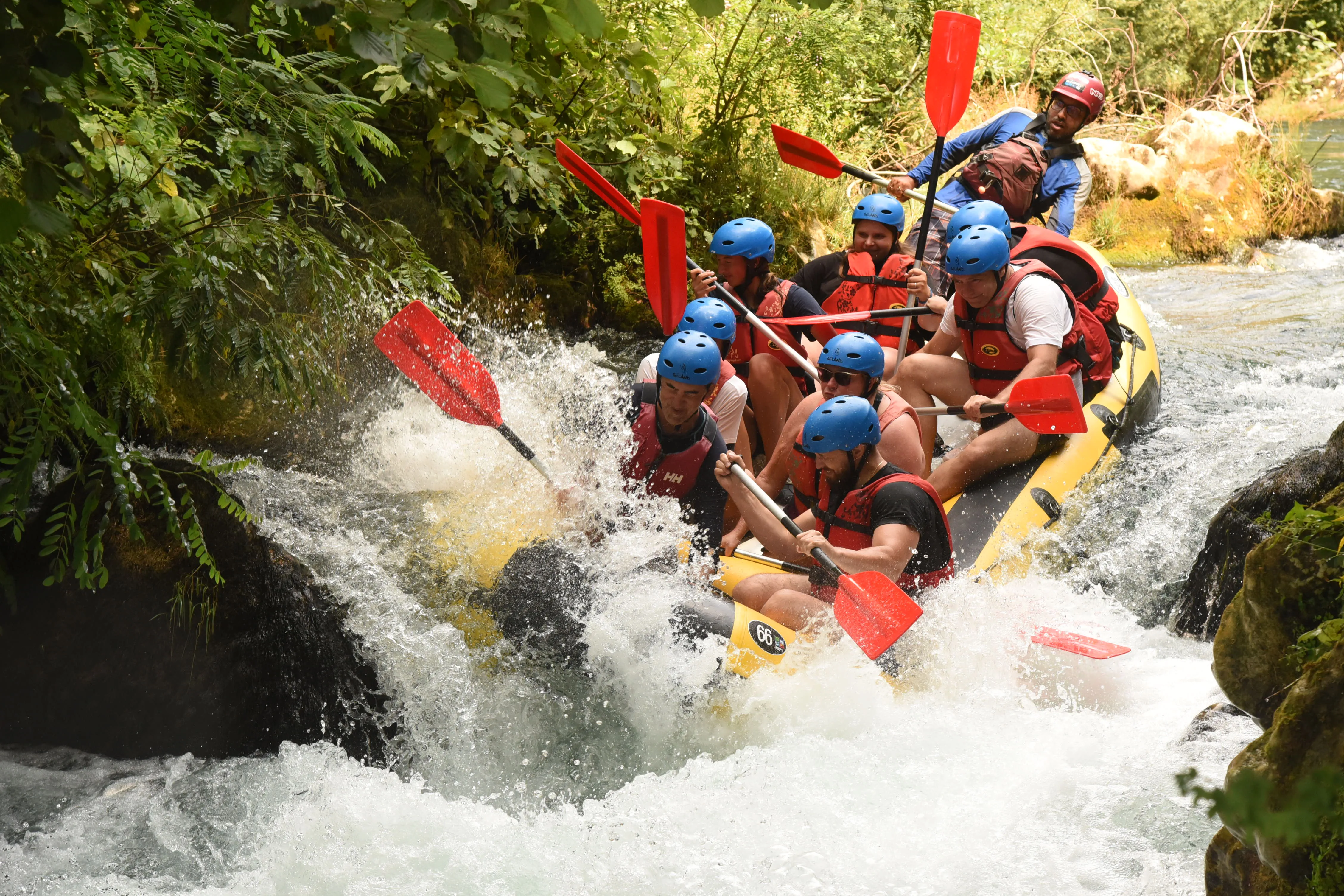 Omis Croatia white water rafting, raft being swept by rapids near rocks slight drop water splashing everywhere, the gymsy traveller at the front with a group of people