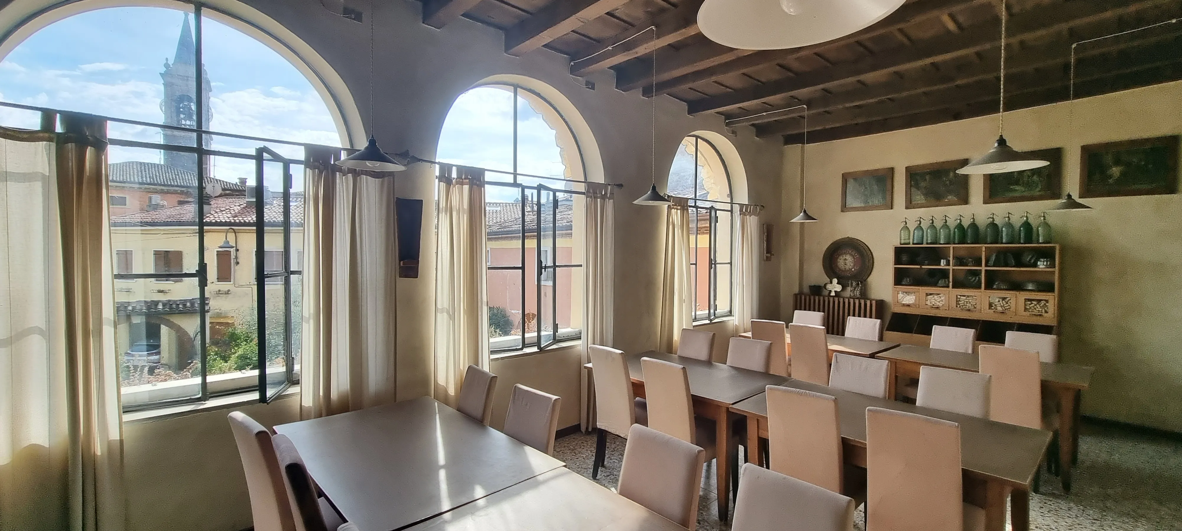 a restaurant we stopped at on the way to verona italy and to the park of waterfalls, room that has sunlight beaming inside three arched windows in rustic look, with outside view of quintessential italian church with bell tower and other buildings surrounding, the gymsy traveller