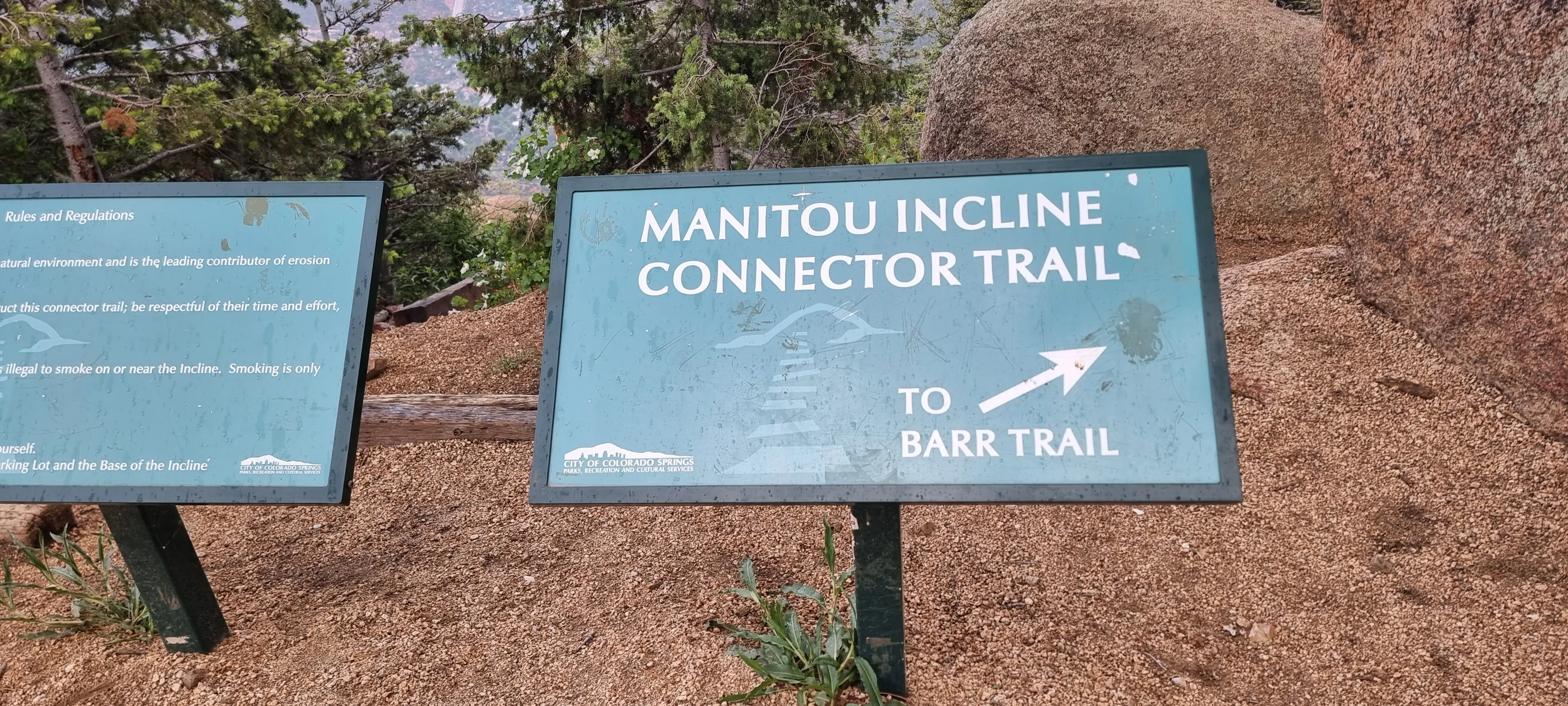A plaque that shows that there is a connector trail off the manitou incline steps that leads to the Barr trail. plaque is placed near rocks and and trees and the top of the summit 