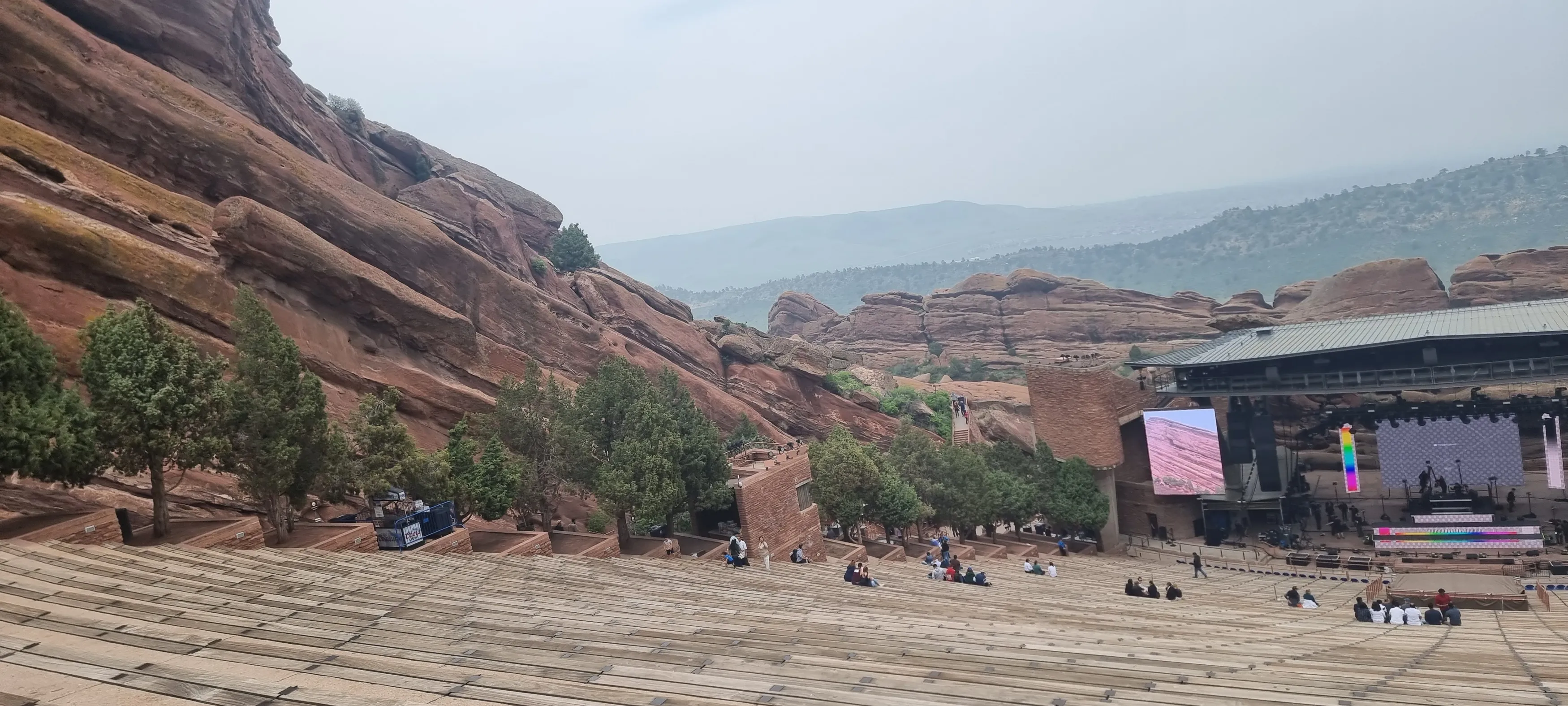 an image of red rocks amphitheatre in colorado, showing the stage doing sound checks at the bottom of the stairs. image taken from top of stairs looking down and the red mountain rocks surrounding the venue. misty day