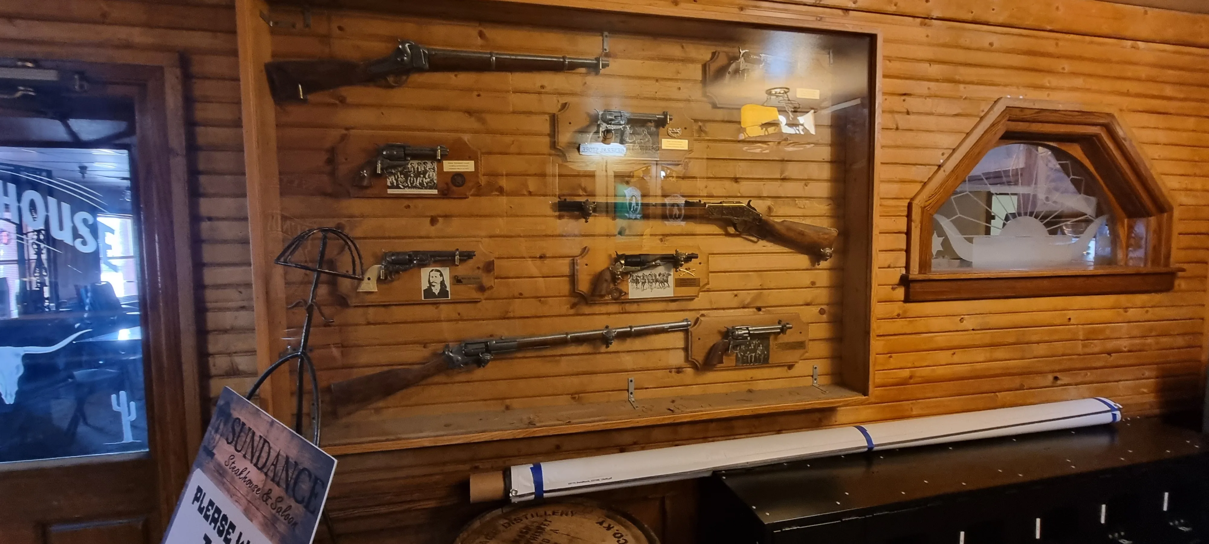 a wooden saloon or bar mantelpiece that shows old guns inside a glass case on the wooden wall