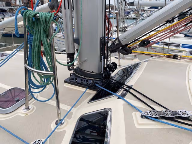 Sailboat deck with mast and various ropes and cables organized around it.