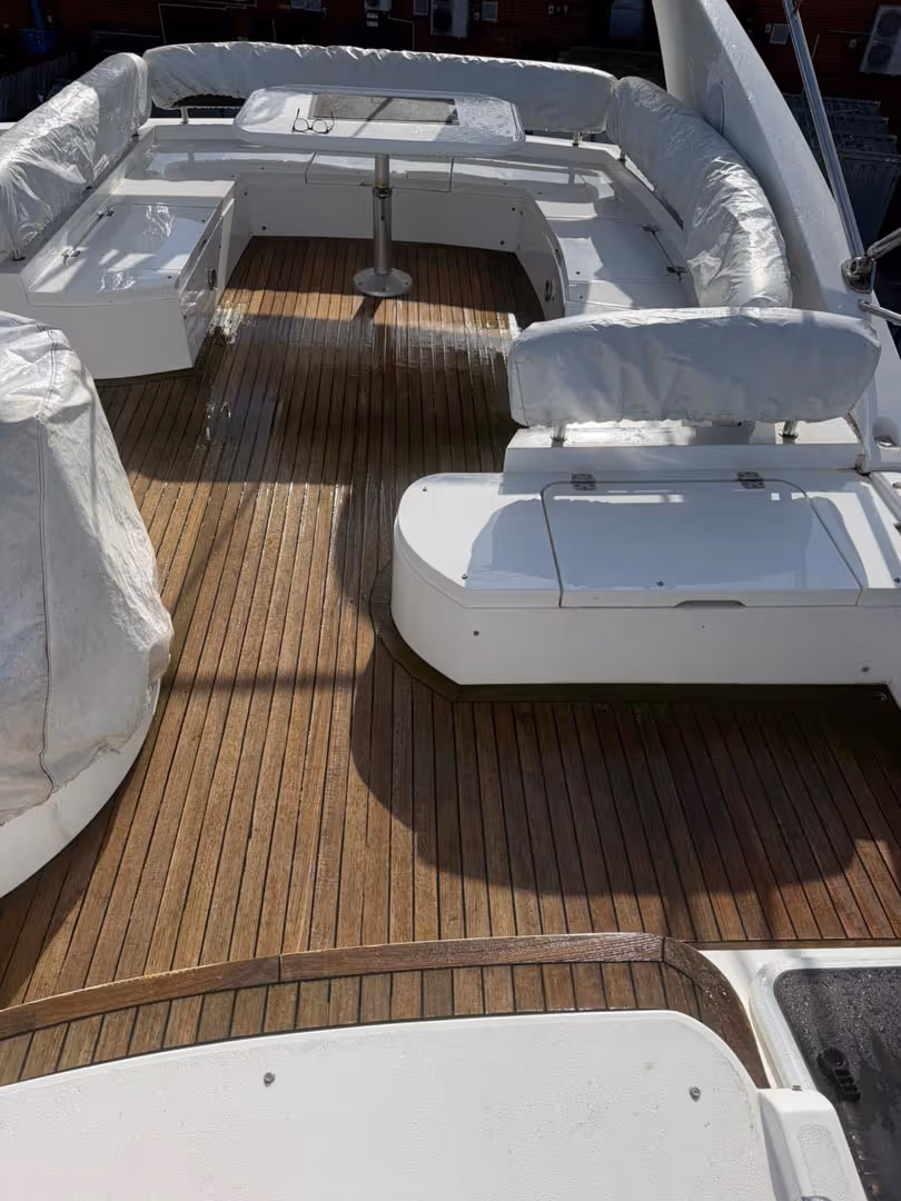 Spacious boat deck with wooden flooring and white cushioned seating arranged in a U-shape.