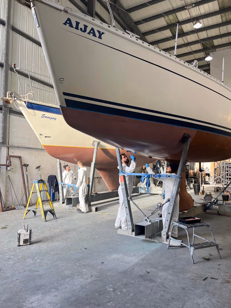 People working on boats in a large indoor facility, focusing on maintenance under the hulls.