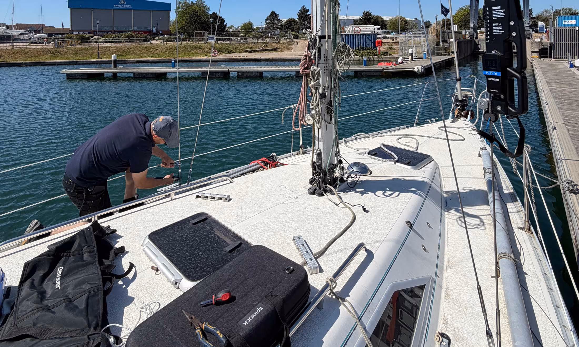 Person adjusting ropes on a sailboat docked in a marina with visible equipment on deck.