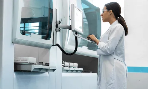 A scientist in a lab coat operates a machine using a touchscreen.