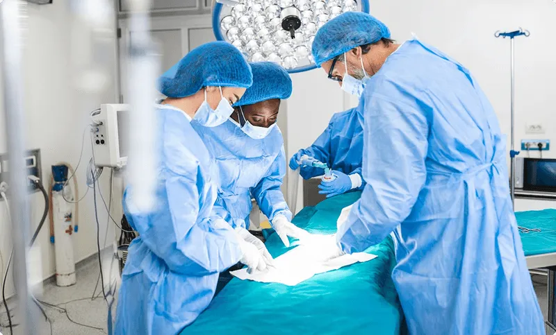 Doctors in blue scrubs perform surgery under bright lights in an operating room.
