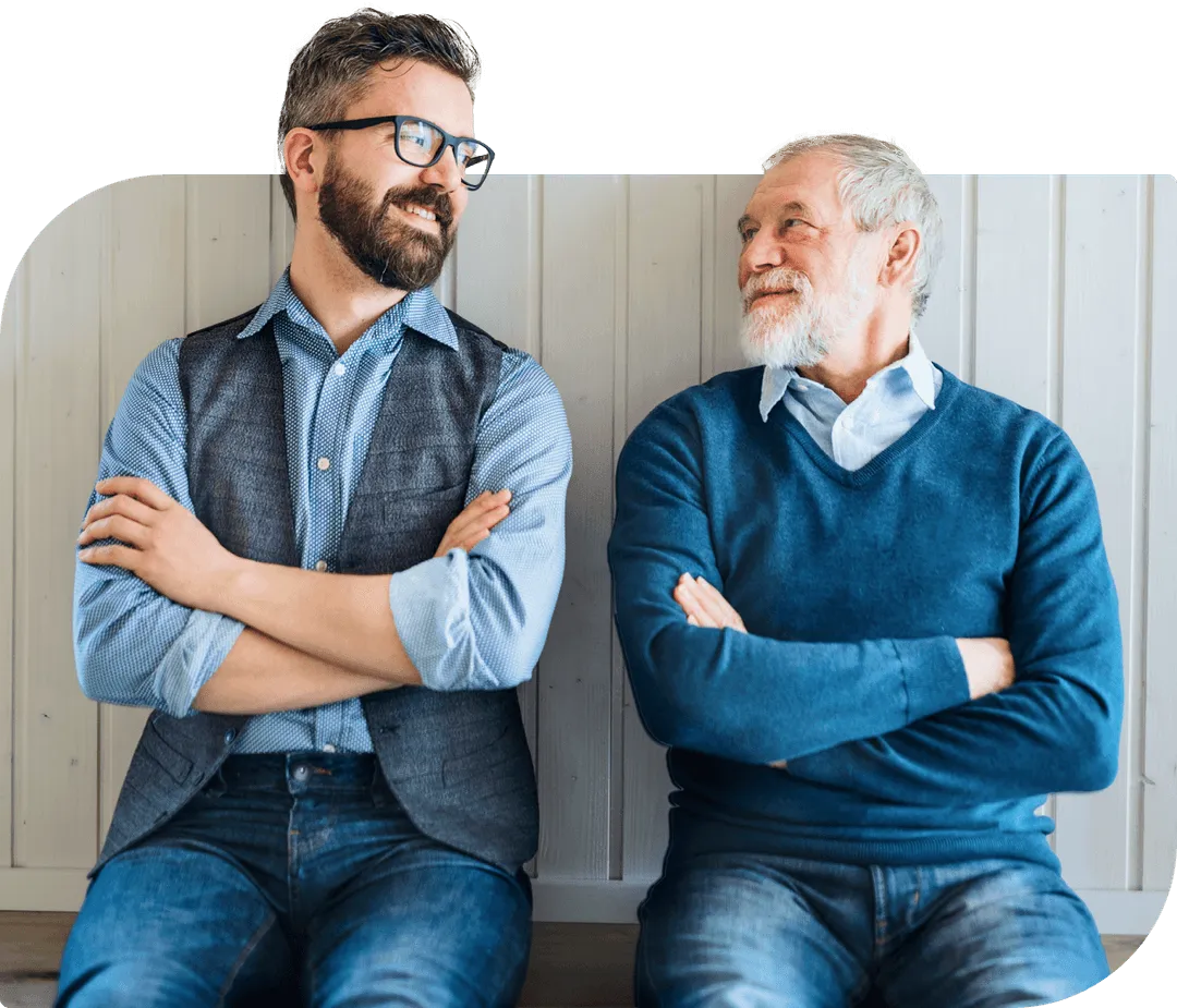 Two men sitting with arms crossed, smiling and looking at each other.