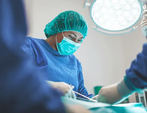 A surgeon in scrubs and mask concentrates on a procedure under bright surgical lights.
