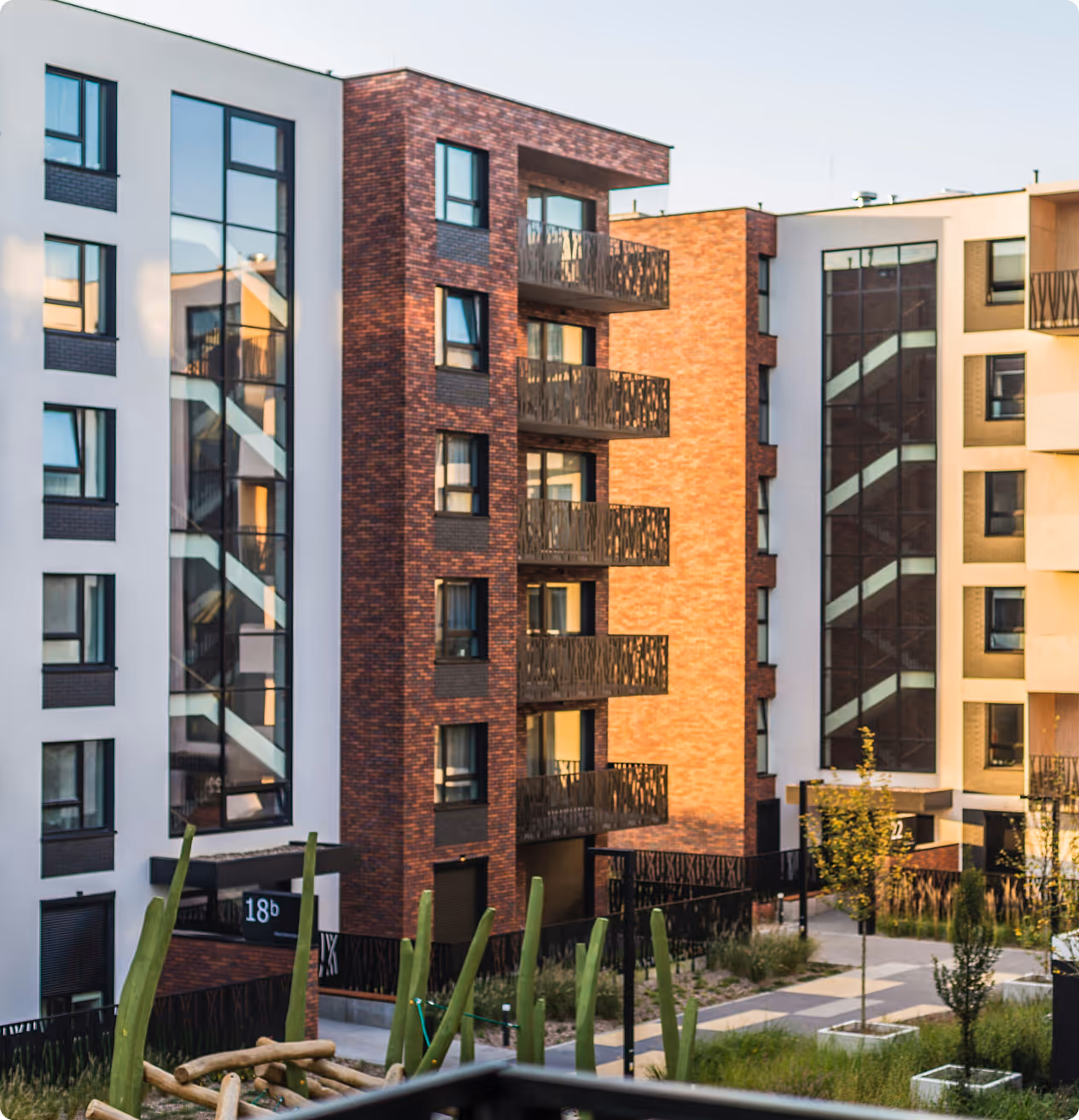 Three modern apartment buildings with large windows and balconies, surrounded by a small landscaped garden.