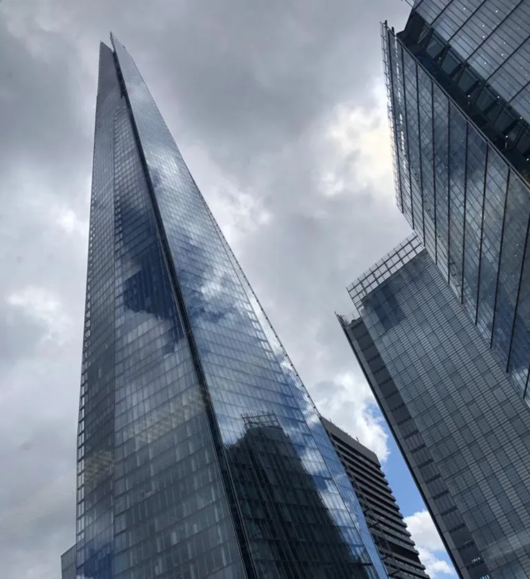 Tall modern glass skyscrapers reflecting cloudy sky from a low angle.