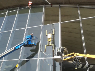 Two workers on lift platforms cleaning the curved glass exterior of a building.