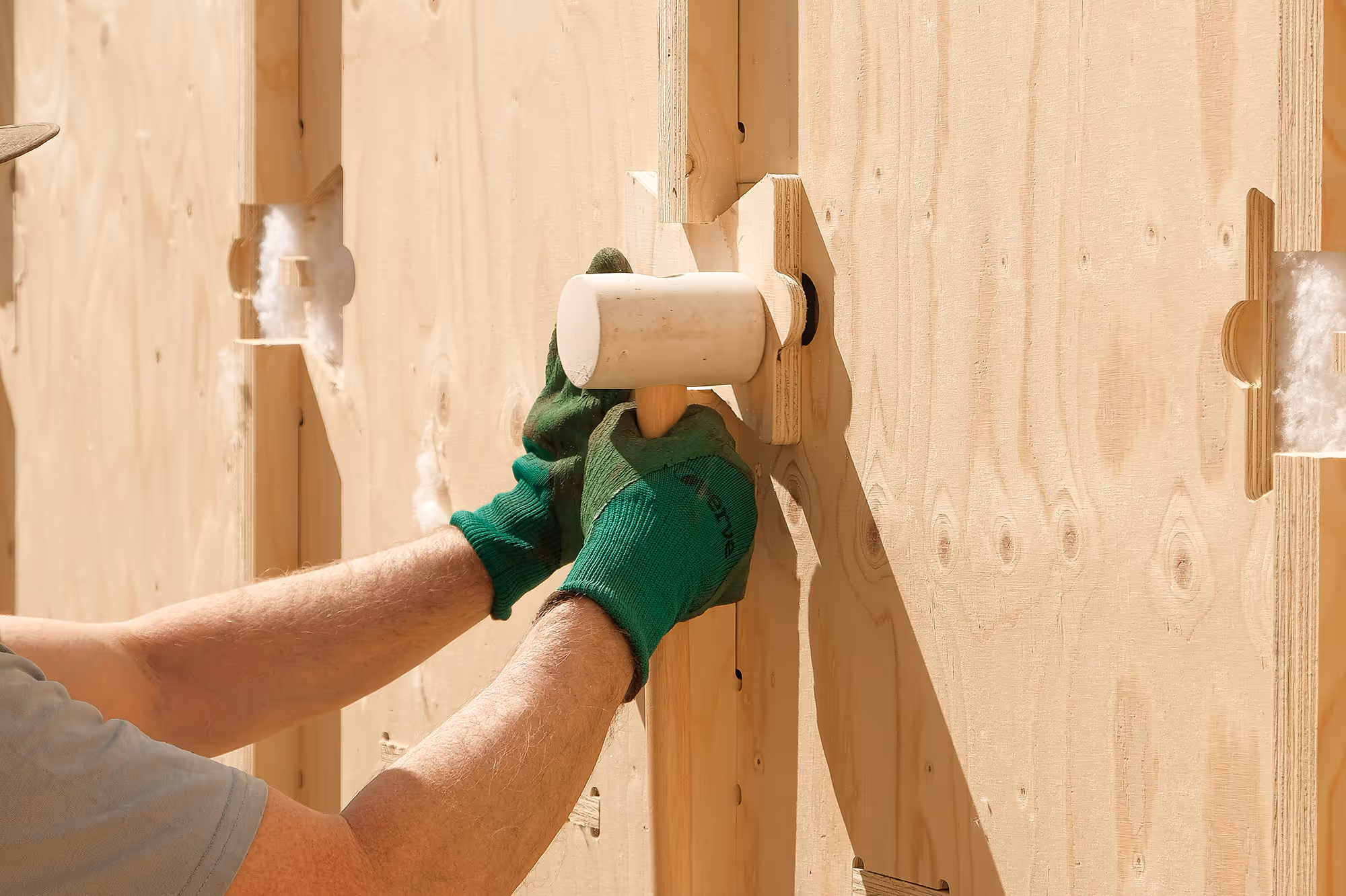A man holding a mallet is tapping 'bow tie' pieces onto a WikiHouse chassis.