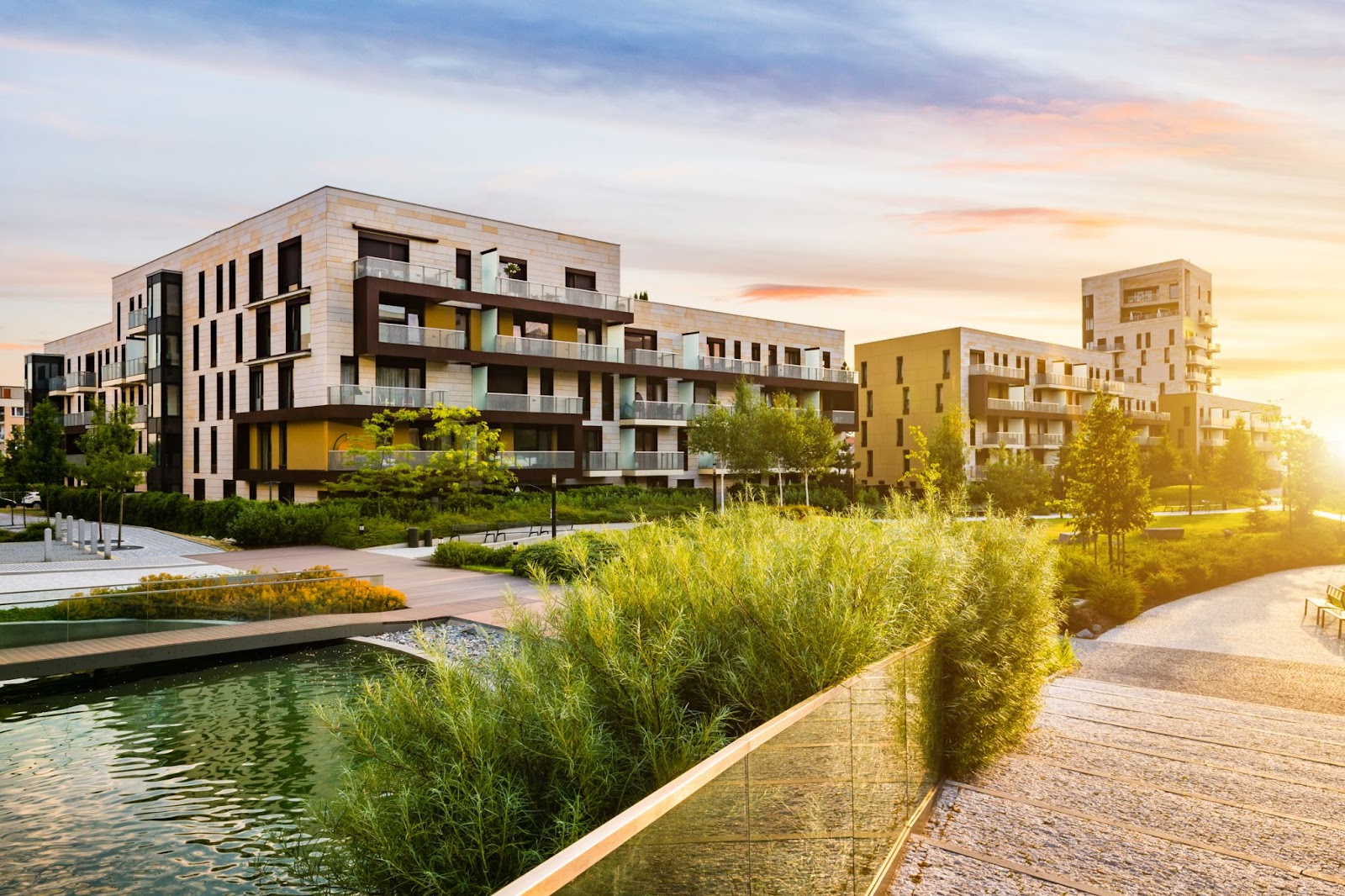 A cluster of modern apartment buildings placed along a canal, surrounded by greenery, photo taken at sunset.