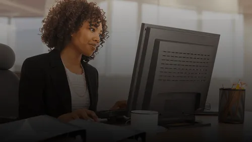 Mujer con cabello rizado trabajando en una computadora de escritorio en una oficina moderna.