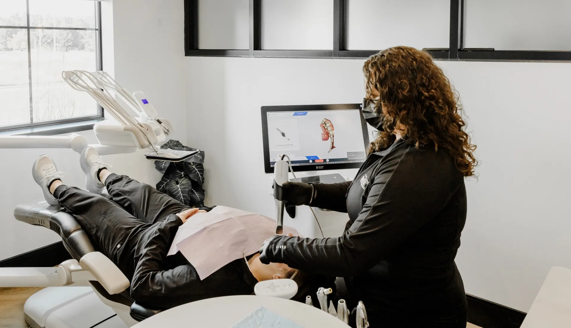 Dental professional wearing black gloves and mask using a handheld scanner on a patient lying in a dental chair.
