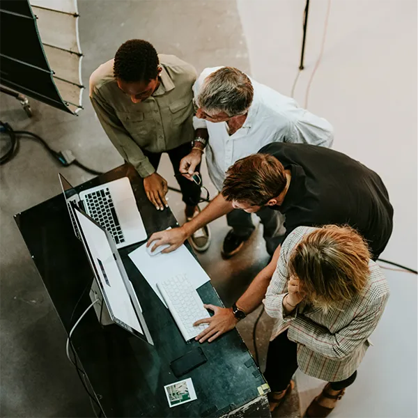 Aerial view of four diverse colleagues gathered closely around a desk working on computers in a modern office.