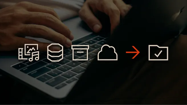Icons representing media files, database, email, cloud storage, an arrow pointing to a folder with a checkmark, over a person typing on a laptop keyboard.