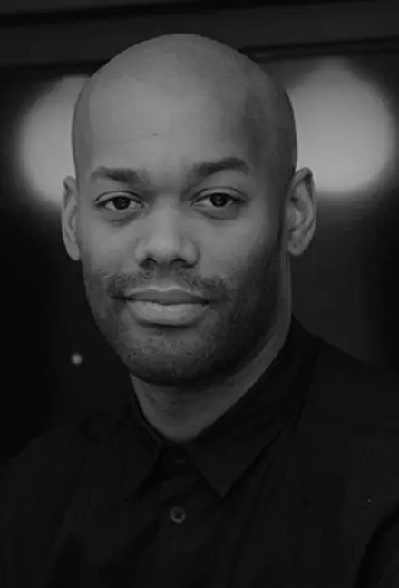 Portrait of a bald man with a trimmed beard, wearing a dark shirt, looking at the camera with a slight smile.