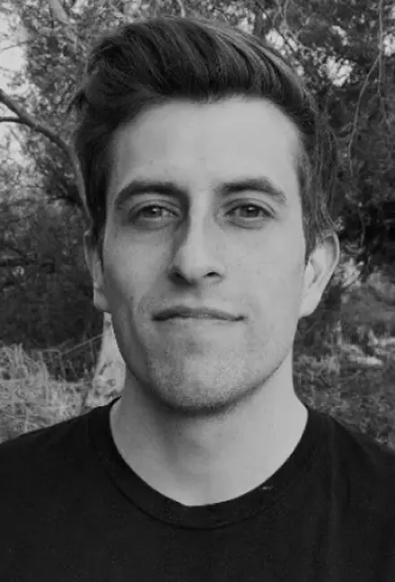 Black and white portrait of a young man with styled hair wearing a dark shirt outdoors.