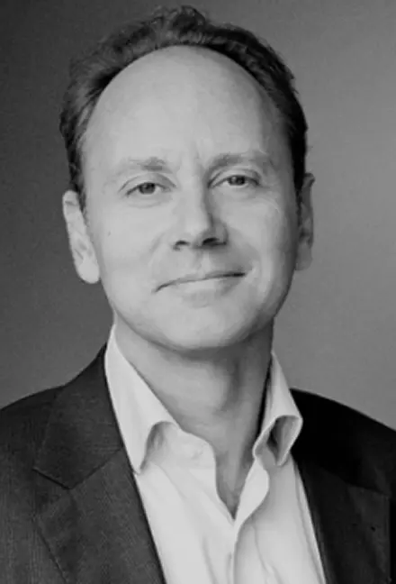 Black and white portrait of a middle-aged man wearing a suit jacket and white shirt, smiling gently.