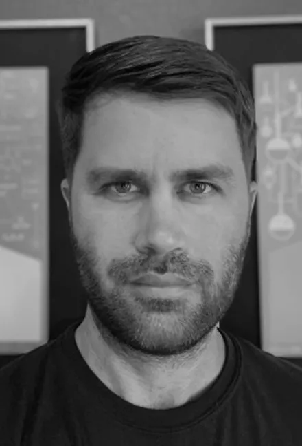 Close-up black and white portrait of a man with short dark hair and a trimmed beard, looking directly at the camera.