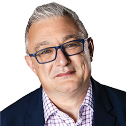 Senior Sales Director, Philip Giles. A man with a small smile and short white hair, wearing glasses and a checkered button-up shirt, under a black suit jacket.