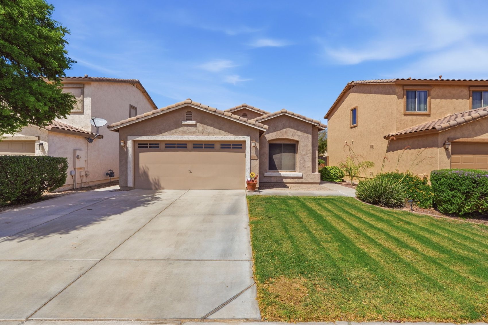 Front of 44840 W Paitilla Lane, a single-story tan stucco home with a two-car garage, tile roof, and a striped green front lawn