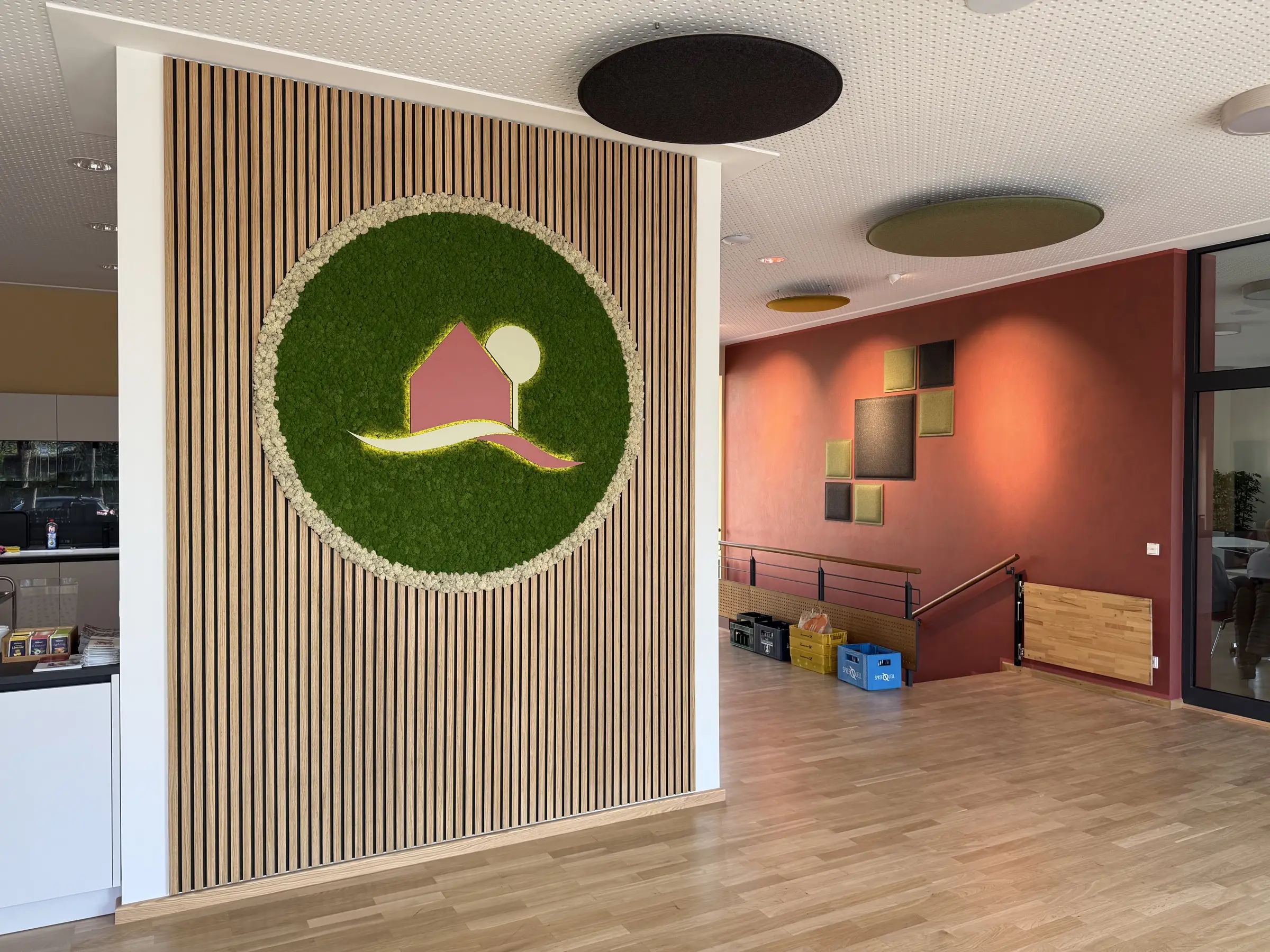Gemeinschaftsbereiche und Veranstaltungsräume der Immobilienverwaltung Märkische Scholle mit Firmenlogo in CI-Farben auf Eichenakustikplatten, die mit Rentiermoos bezogen sind.