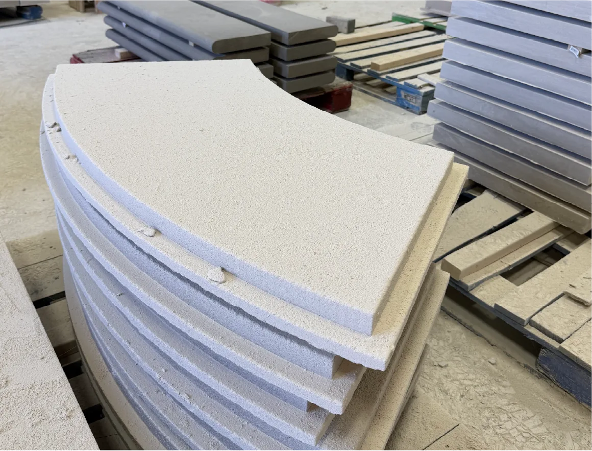 Radius-cut limestone wall coping pieces stacked in a fabrication shop