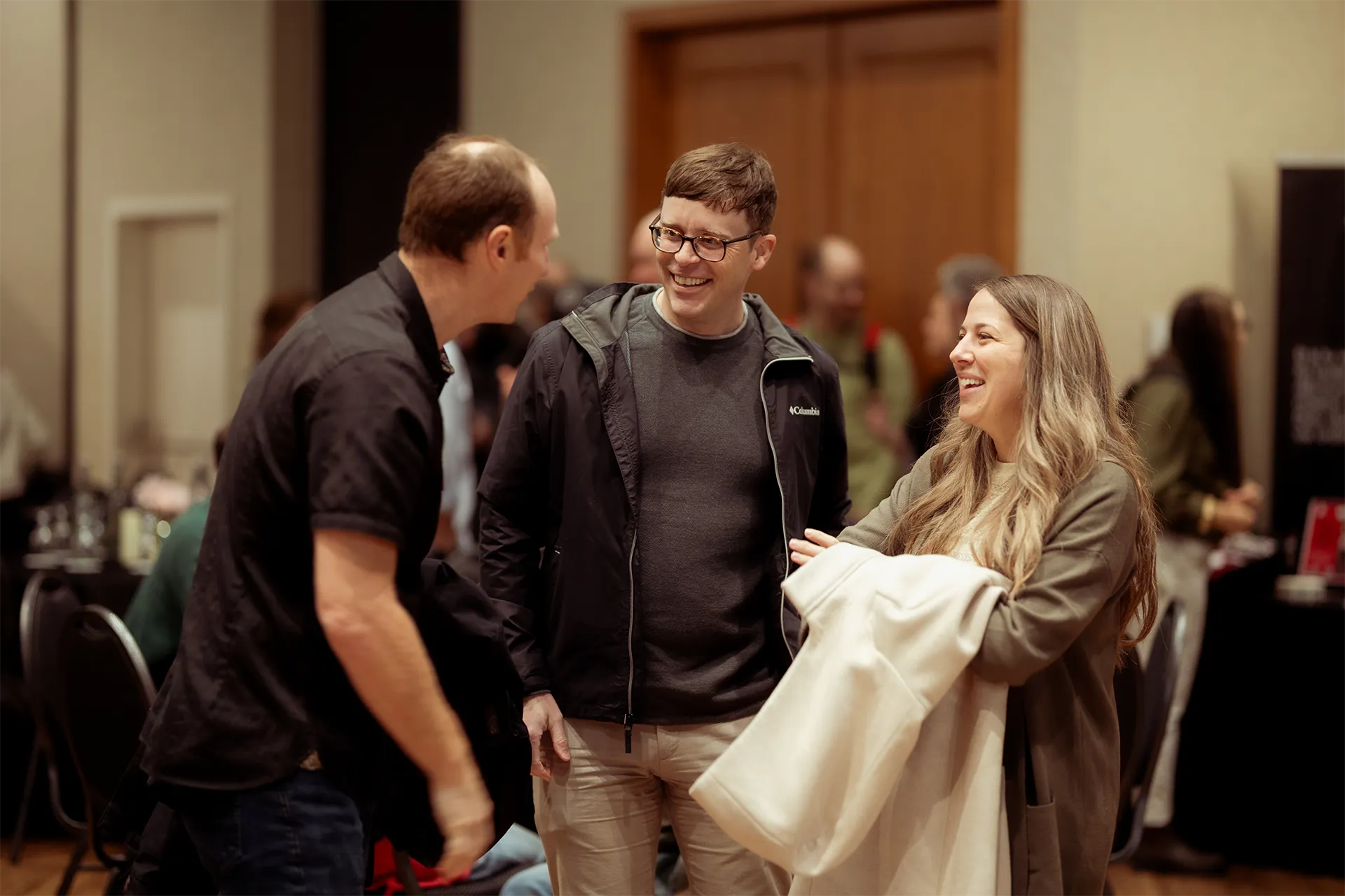 Trois personnes souriant et discutant à l’intérieur lors d’un événement