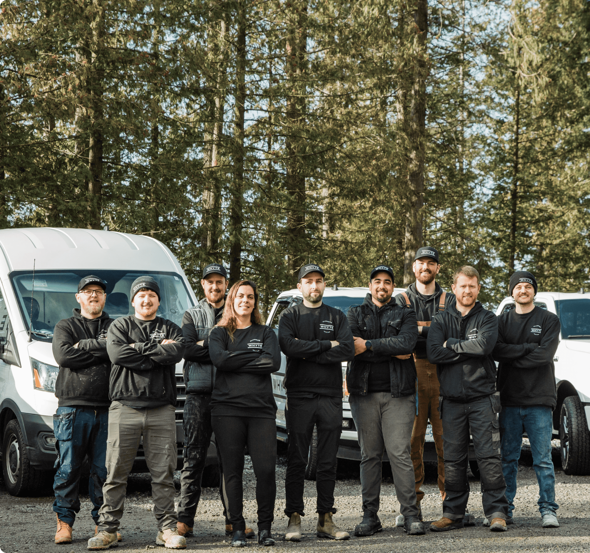 Nine workers in black Whyte Apparel, standing outdoors with white vans and trees behind them.