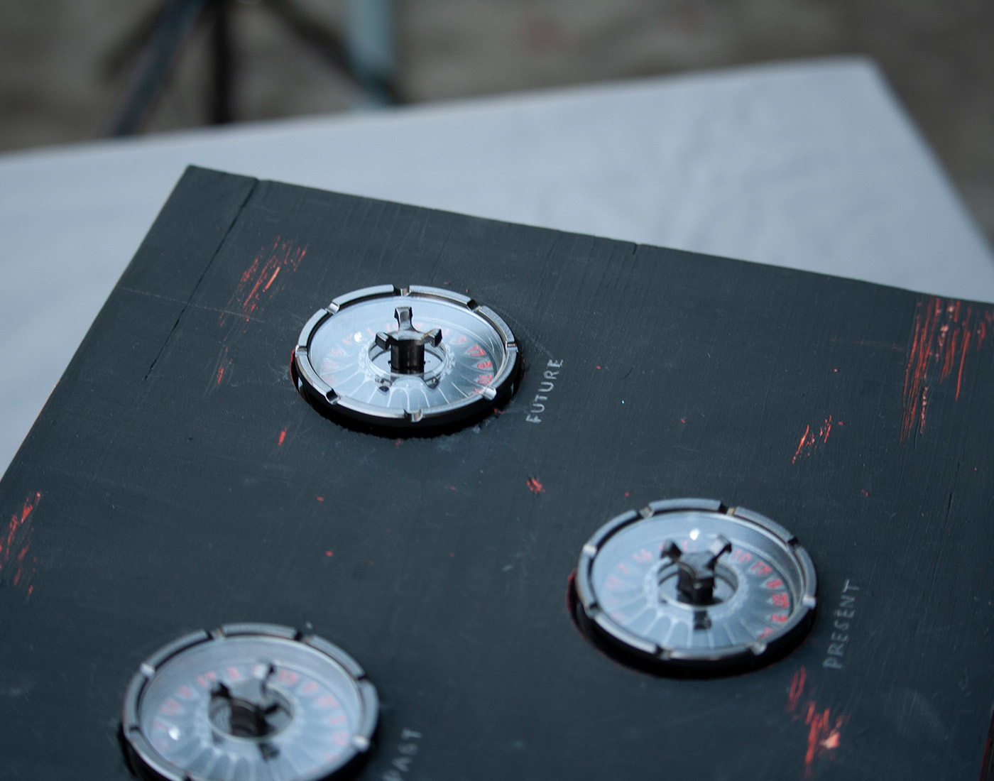 Dark metallic dials on black wooden box are labeled "past, present, future"