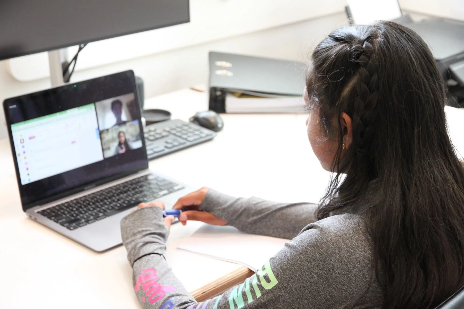 Student writing in her workbook during a live online lesson, her teacher on screen