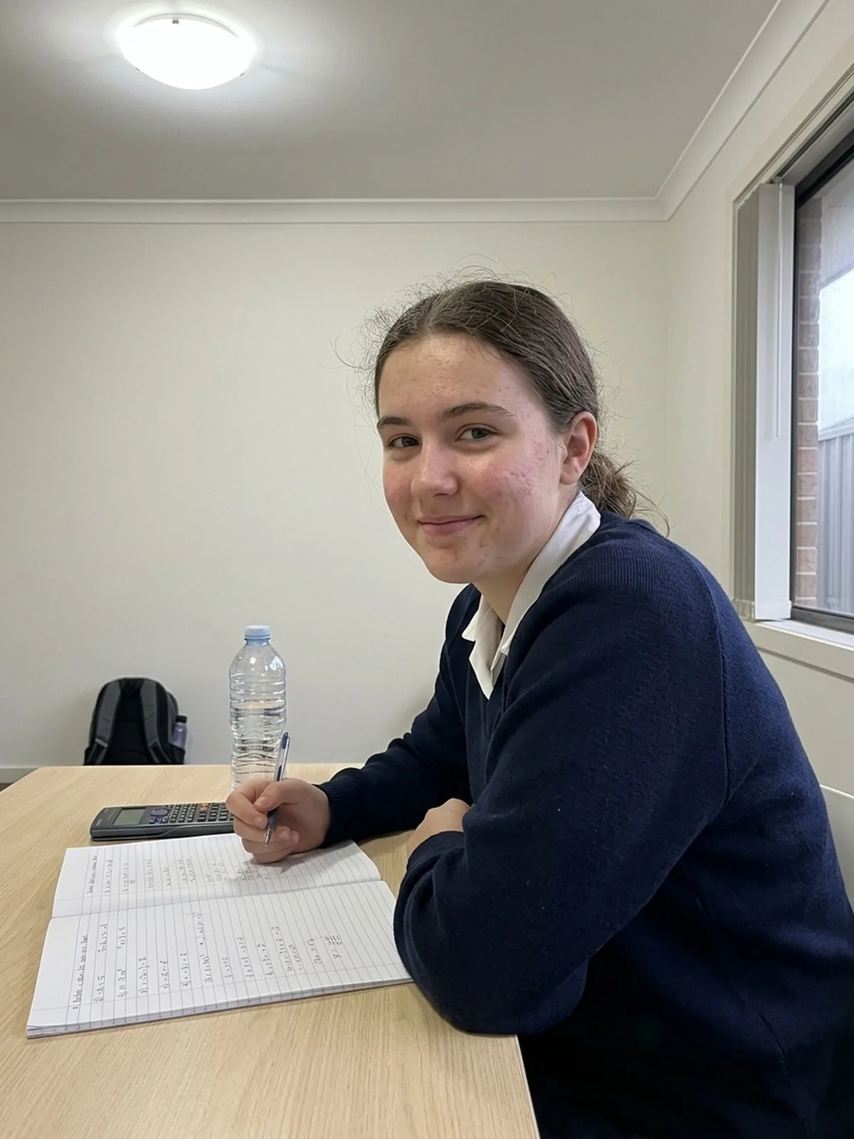 Senior student working through her book at home, calculator beside her