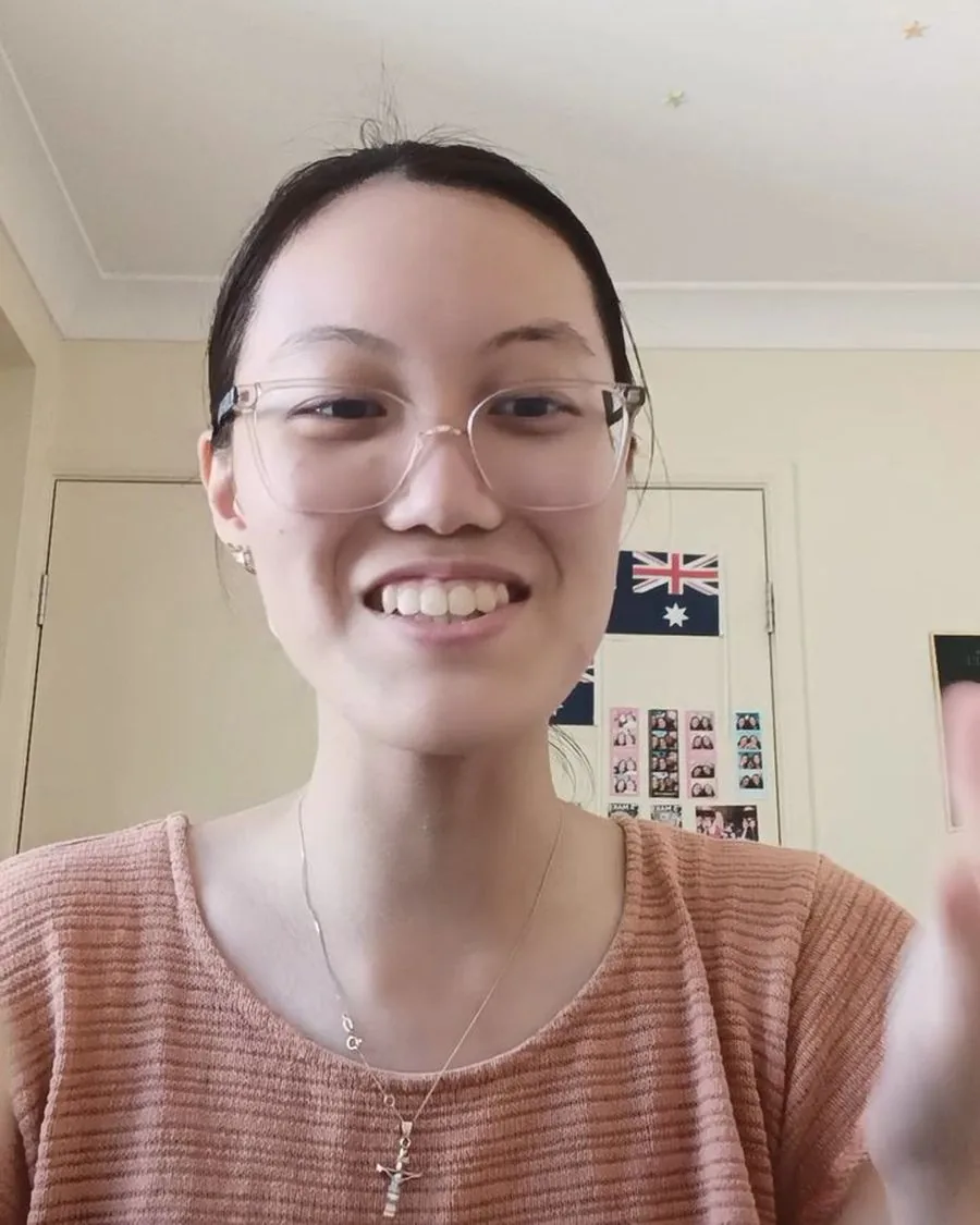Elena smiling on a video call from her bedroom, an Australian flag on the wall behind her